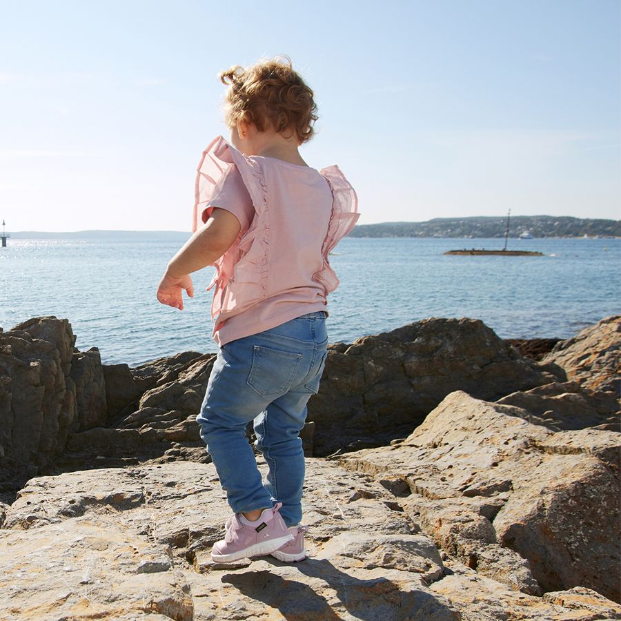 A hiker wearing the VIKING GORE-TEX Halbschuh VEME GTX - flieder while crossing a stream, demonstrating the waterproof capabilities of the shoe