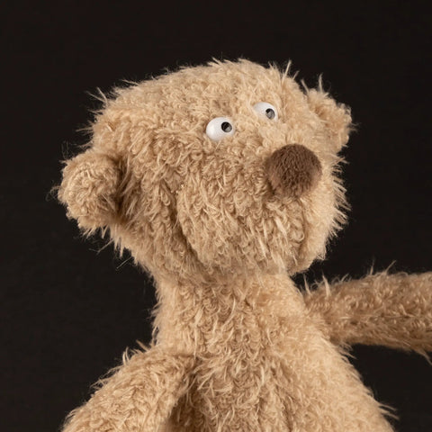 Stofftier Bär: Nahaufnahme eines flauschigen braunen Plüschtiers mit großen weißen Augen vor dunklem Hintergrund