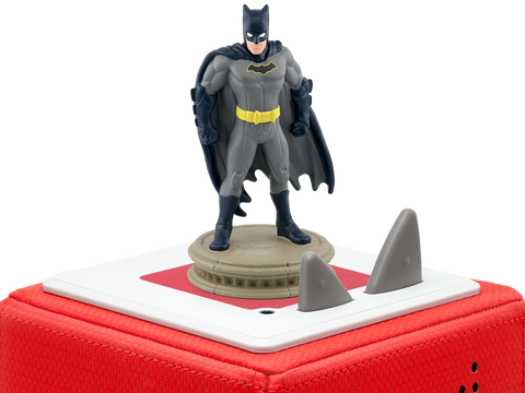 Vorderansicht: TONIES Batman-Figur im grauen Anzug, gelber Gürtel, auf beigem Sockel vor rotem Tonie-Boxgehäuse.