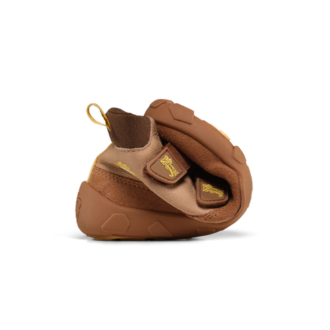 Detailaufnahme: brauner AFFENZAHN TEX Knöchelschuh mit Klettverschluss, goldenen Logos und gelber Fersen-Schlaufe.