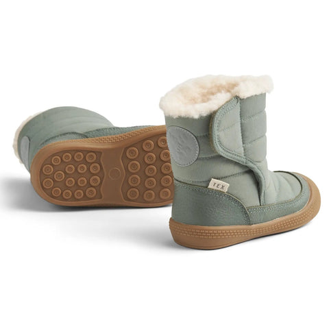 Seitenansicht des WHEAT Stiefel DELANEY WF389-01 in Salbei mit Fellrand und brauner Gummisohle.